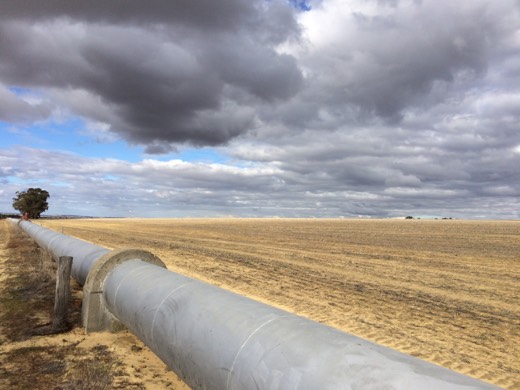 The water pipeline running beside open paddocks under a dramatic sky on Day 3