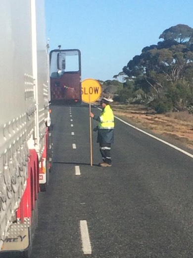 A traffic controller holding a slow sign beside queued trucks on Day 27.