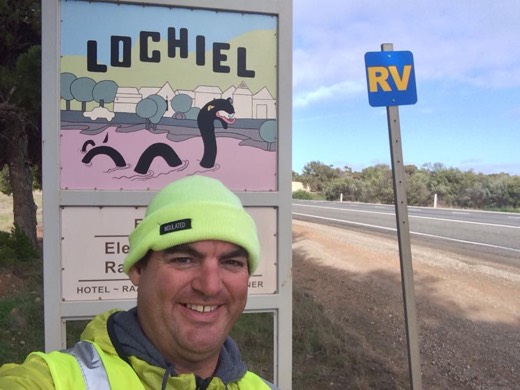 Gary at the Lochiel sign beside the pink lake and Nessie artwork.