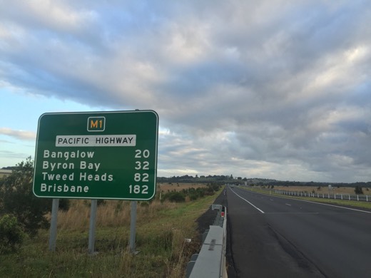 A Pacific Highway distance sign showing Byron Bay 32 kilometres and Brisbane 182 kilometres.