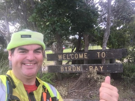 Gary smiling beside the Welcome to Byron Bay sign on Day 119.
