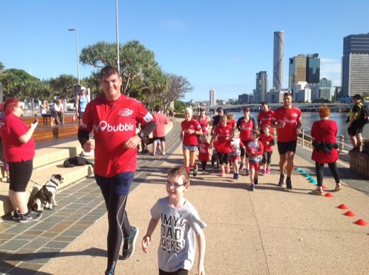 Gary running beside his son at South Bank with other parkrunners behind them.