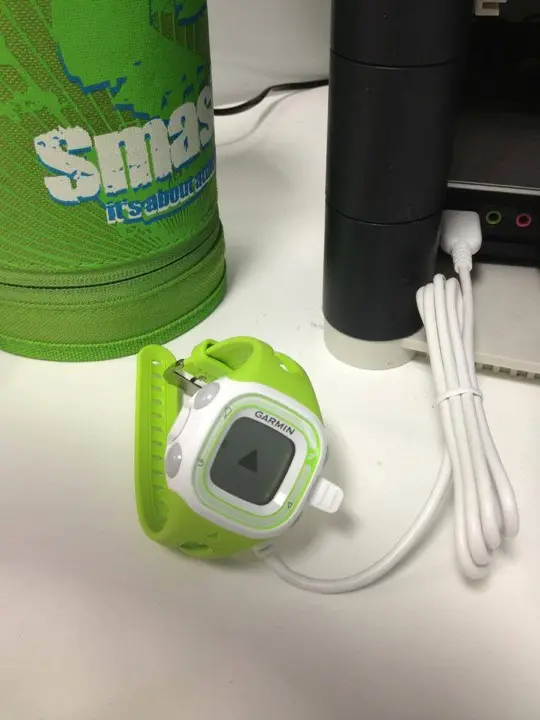 A green Garmin Forerunner 10 watch charging beside a no more mr fat guy water bottle